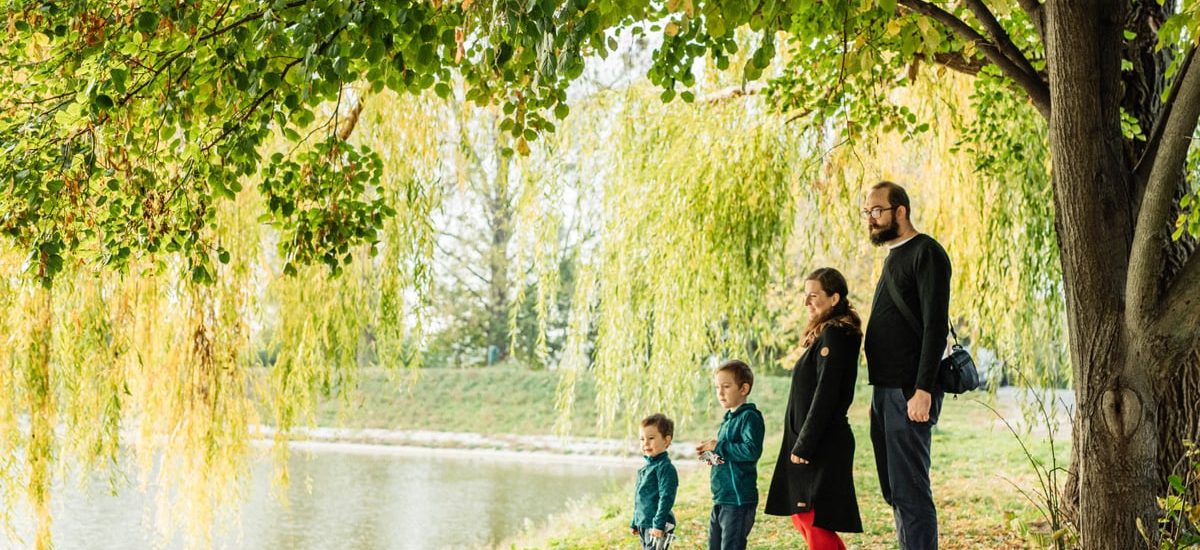 A family enjoys a peaceful walk by a lakeside under a willow tree during autumn.