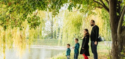 A family enjoys a peaceful walk by a lakeside under a willow tree during autumn.