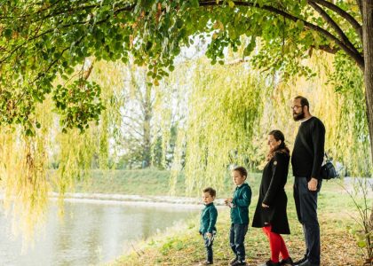A family enjoys a peaceful walk by a lakeside under a willow tree during autumn.