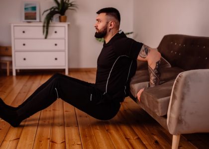 A bearded man in black fitness attire exercising at home, showcasing arm tattoos and a healthy lifestyle.
