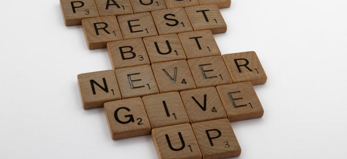 Wooden tiles spelling out 'Pause Rest But Never Give Up' on a white background.