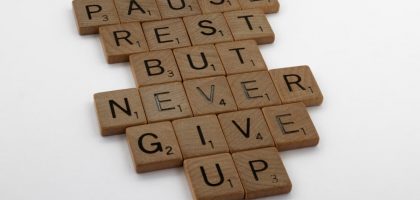 Wooden tiles spelling out 'Pause Rest But Never Give Up' on a white background.