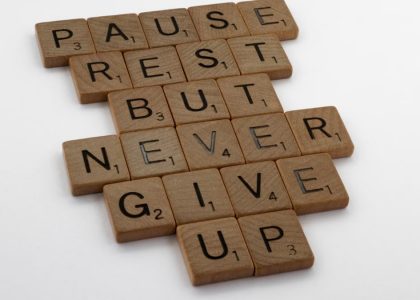 Wooden tiles spelling out 'Pause Rest But Never Give Up' on a white background.